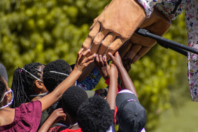 Little Amal holding hands with children at Boschendal Farm in South Africa